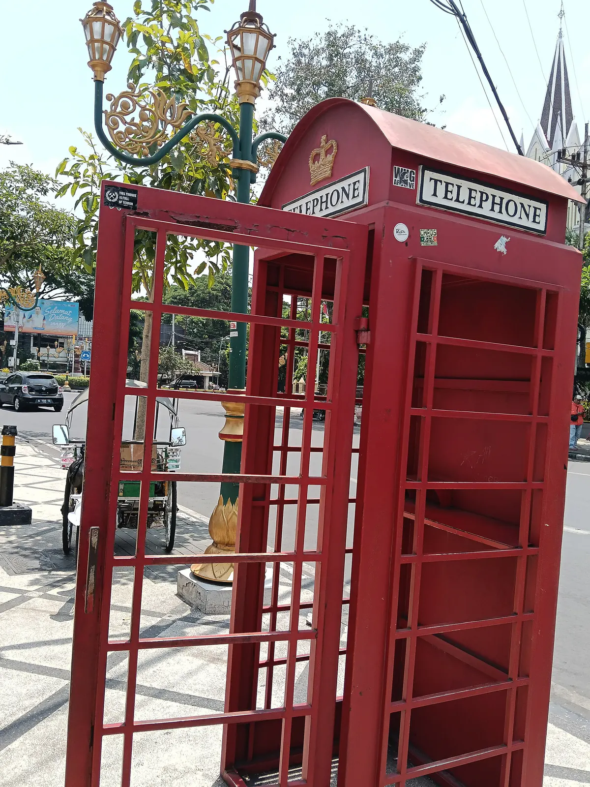 Boks telepon merah bergaya Inggris di trotoar Jalan Basuki Rahmat dengan menara gereja di latar