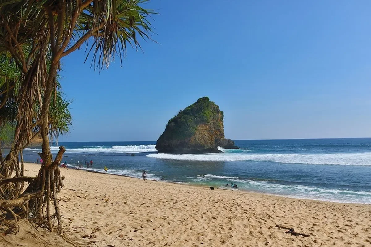 Pasir putih, pohon pandan, dan batu karang besar di Pantai Ngudel, Gedangan, Kabupaten Malang