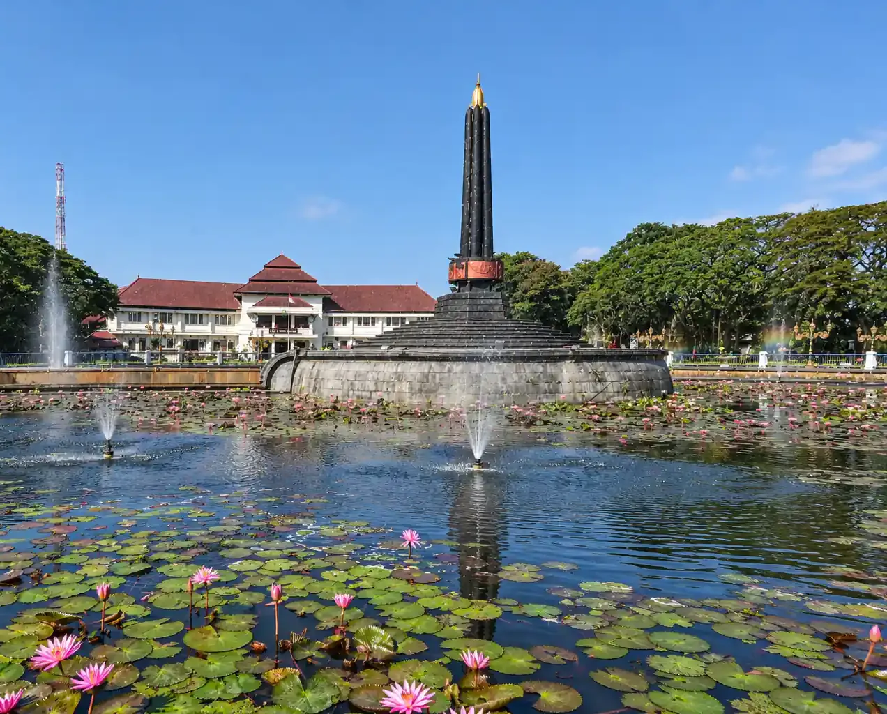 Tugu Malang berdiri di tengah kolam teratai dan air mancur Alun-alun Tugu, dengan Balai Kota Malang di belakangnya