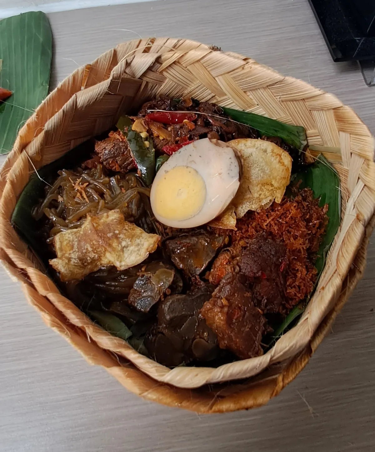 Nasi campur Madura dengan telur pindang, empal, serundeng, dan kerupuk dalam wadah anyaman