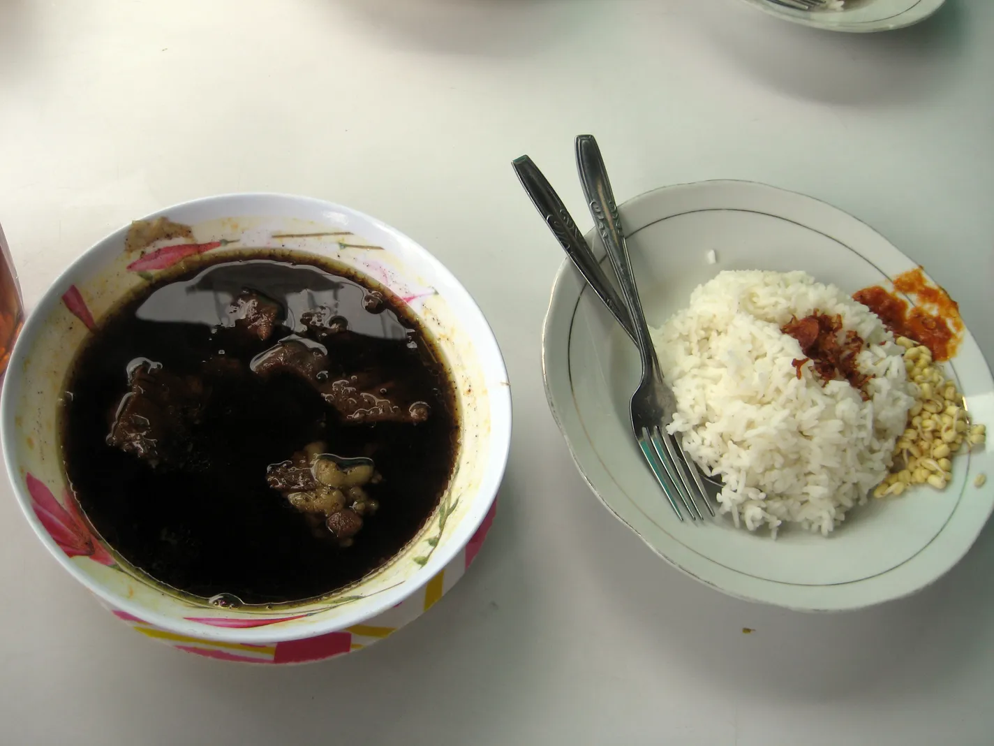 Semangkuk rawon berkuah hitam dan sepiring nasi dengan tauge di Rawon Setan Surabaya