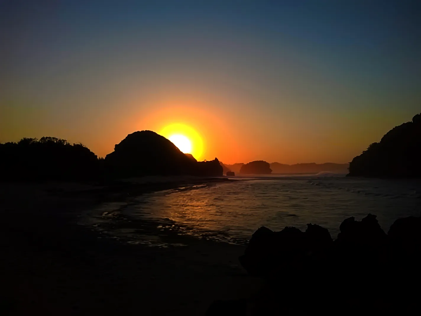 Matahari terbit di balik bukit karang, siluet pulau di Pantai Goa Cina