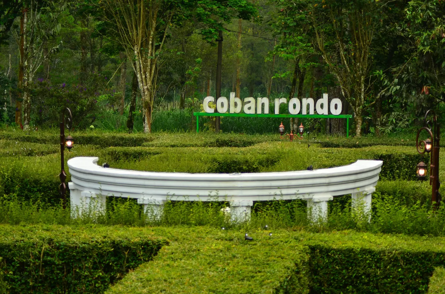 Taman labirin pagar tanaman dengan bangku melengkung putih dan papan nama di belakangnya